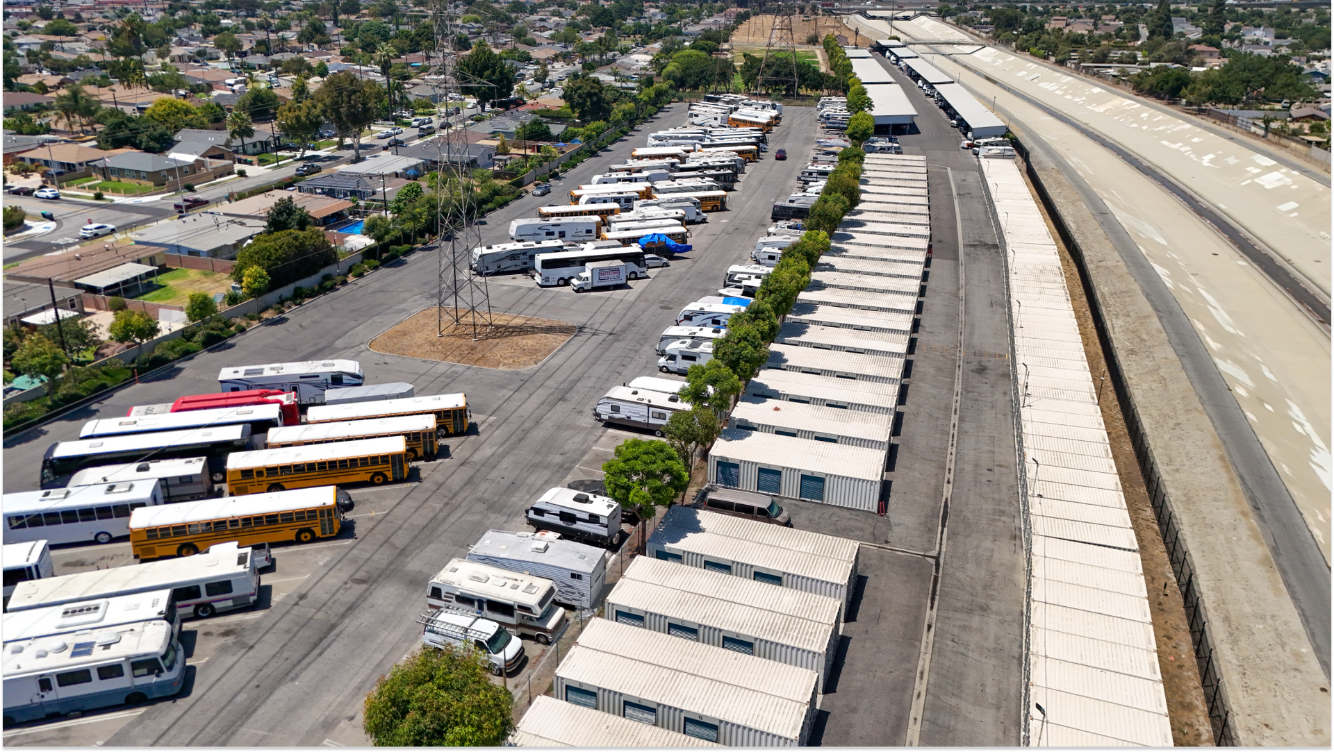 Aerial image of various busses and cars in the parkikng lot near storage units