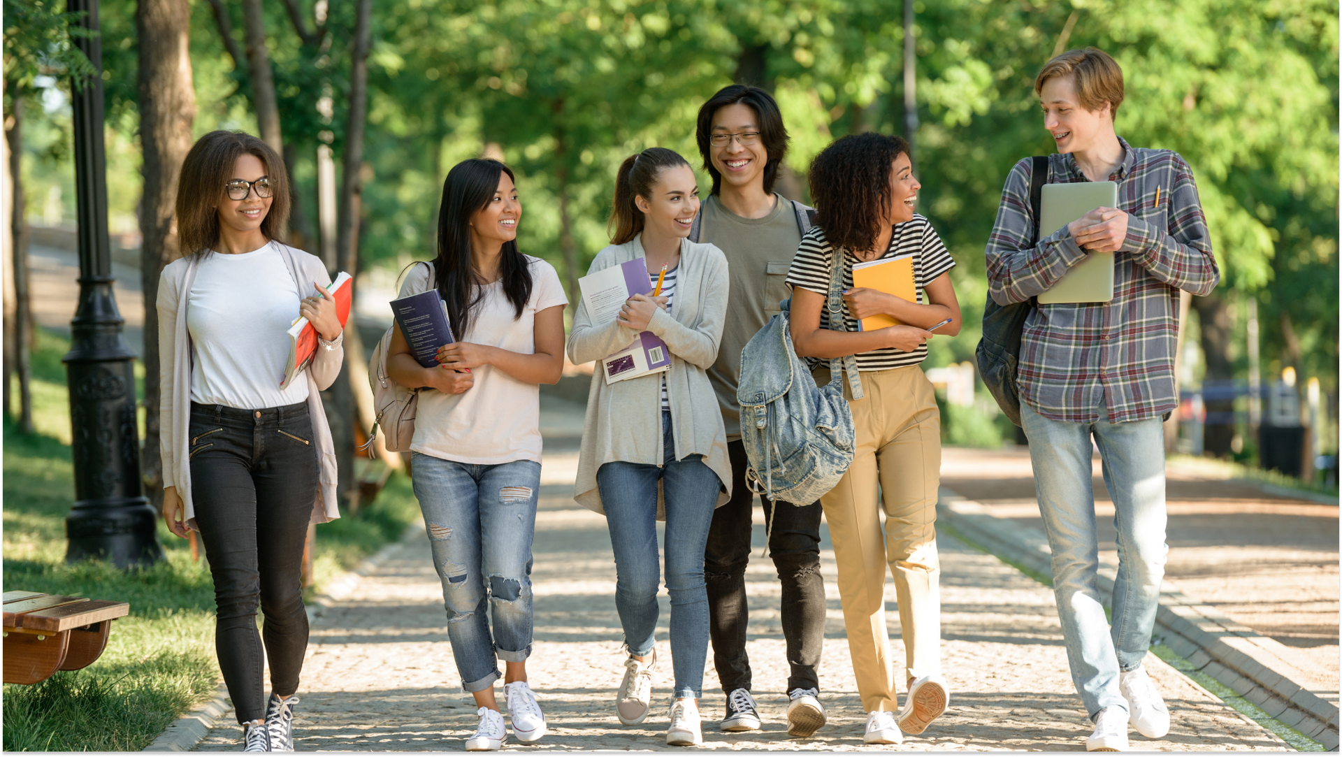 students in various clothing walking in a park holding study materials