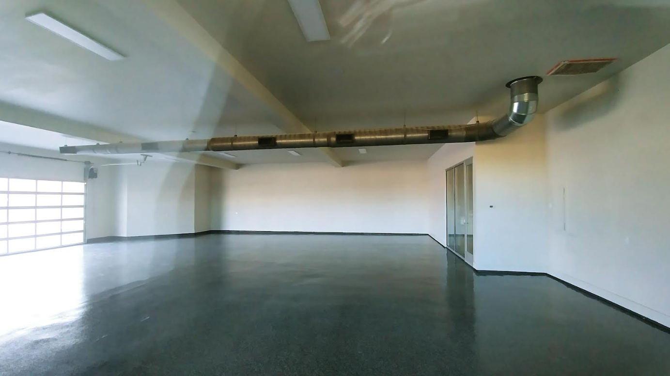 Empty industrial room with white walls, dark polished floor, exposed ceiling ducts, and large window on the left