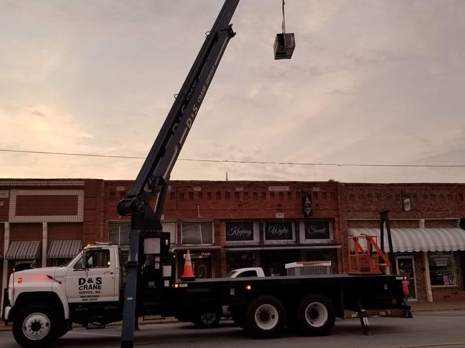 Crane truck lifting a bucket in front of storefronts at dusk