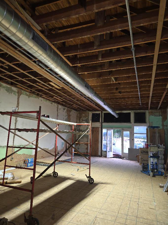 Interior under renovation with exposed ceiling beams, scaffolding, and glass doors at the far end.