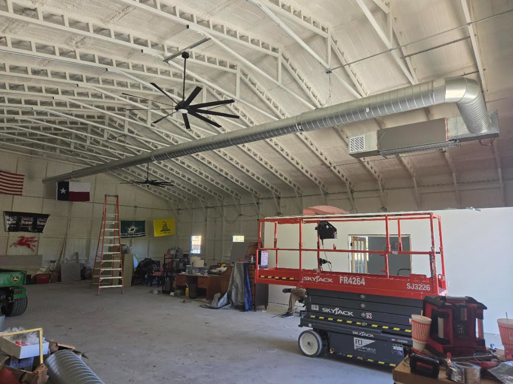 Warehouse interior with a red scissor lift, tools, and a large ceiling fan on the curved roof