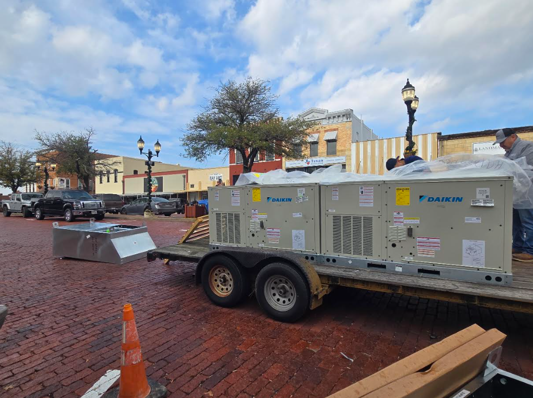 Large gray utility trailer and equipment on a wet brick plaza under cloudy skies