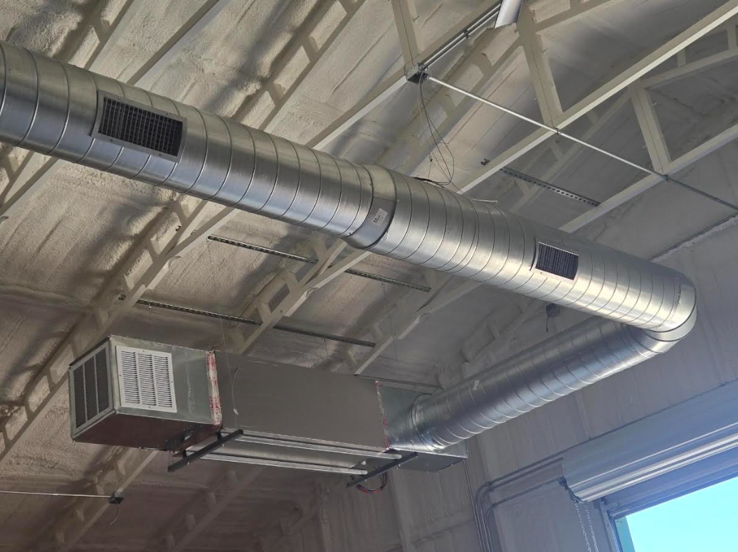 Industrial ceiling with silver HVAC ductwork and a wall-mounted unit near a window