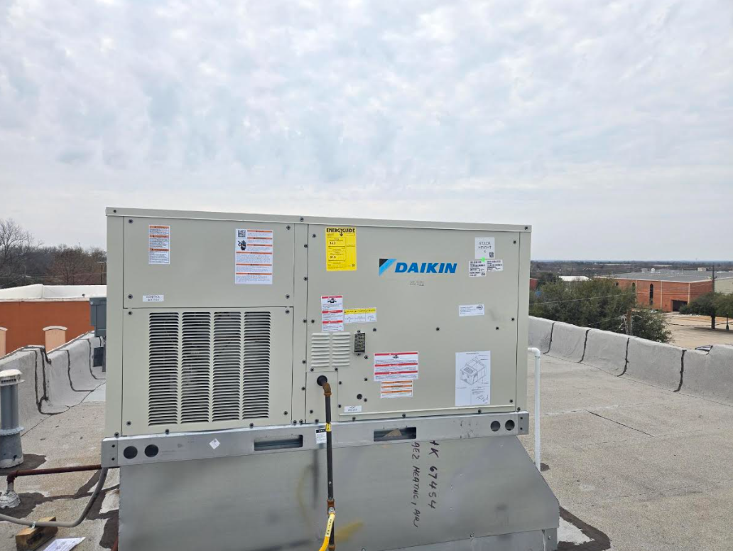 Rooftop HVAC unit with rooftop ductwork under a cloudy sky.