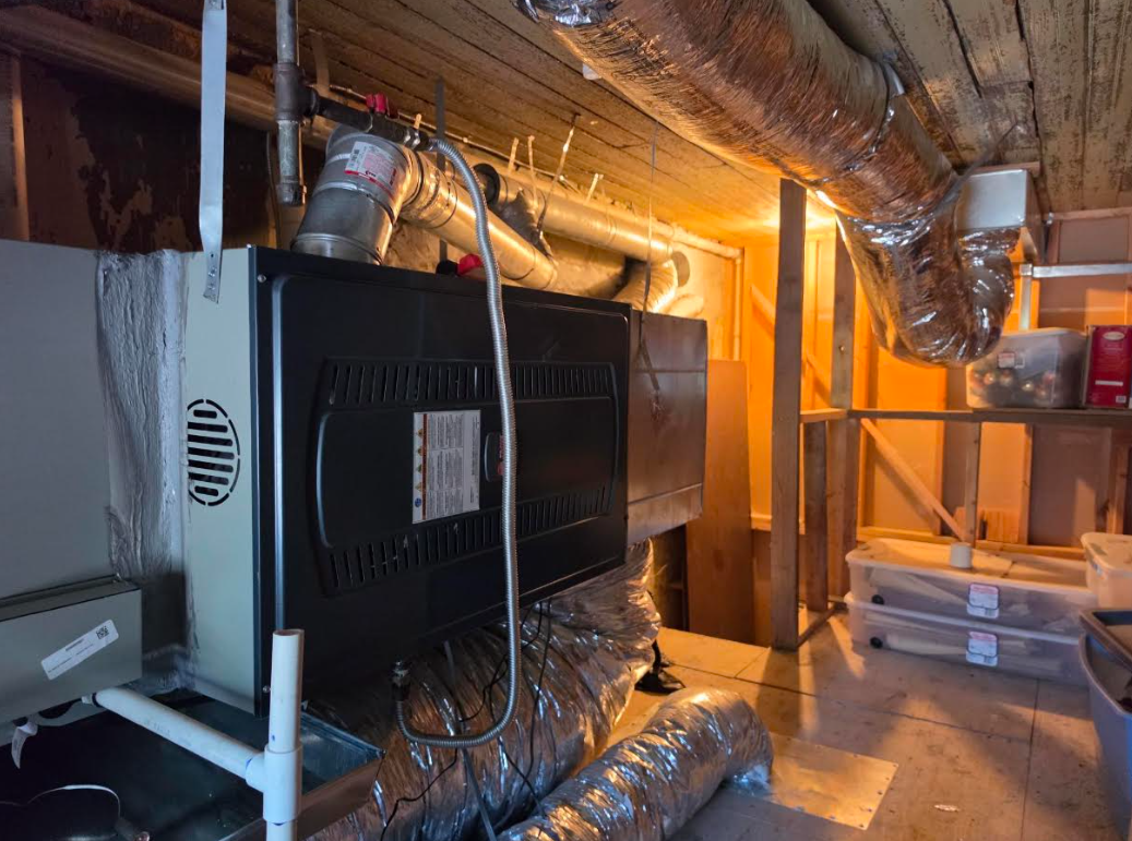Ductwork and a large black HVAC unit in a mechanical room with reflective insulation and warm lighting