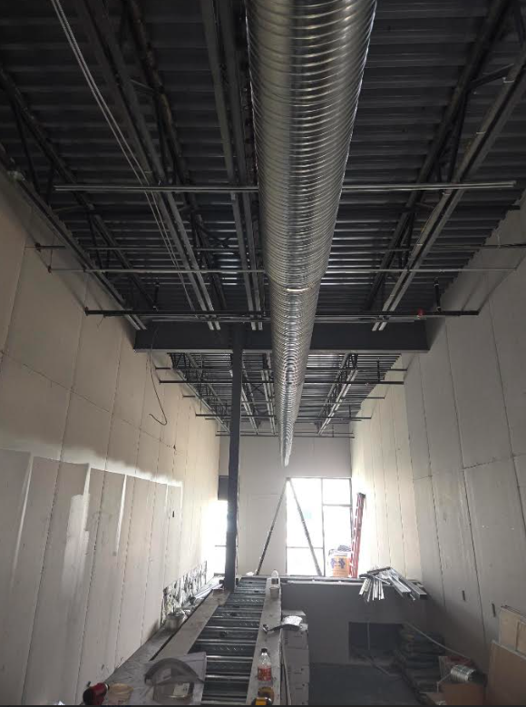 Interior of a construction site with exposed ceiling ducts, unfinished walls, and scaffolding in a long corridor