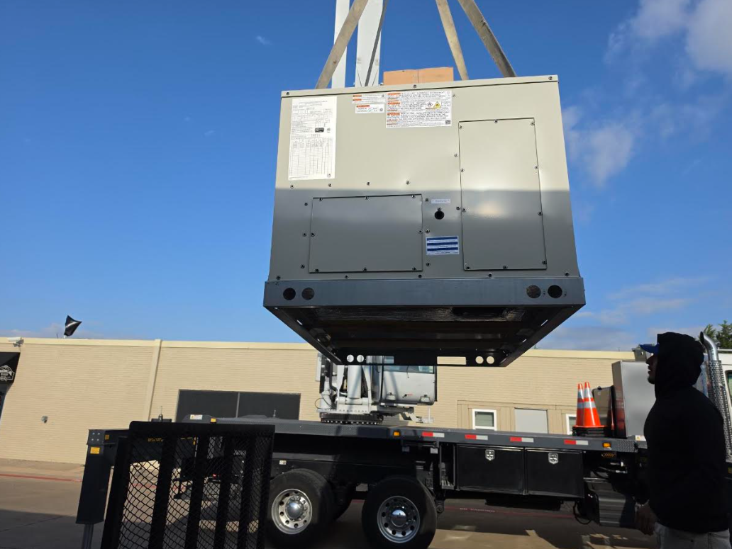 Large gray industrial unit being lifted by straps onto a trailer in an outdoor lot under a blue sky