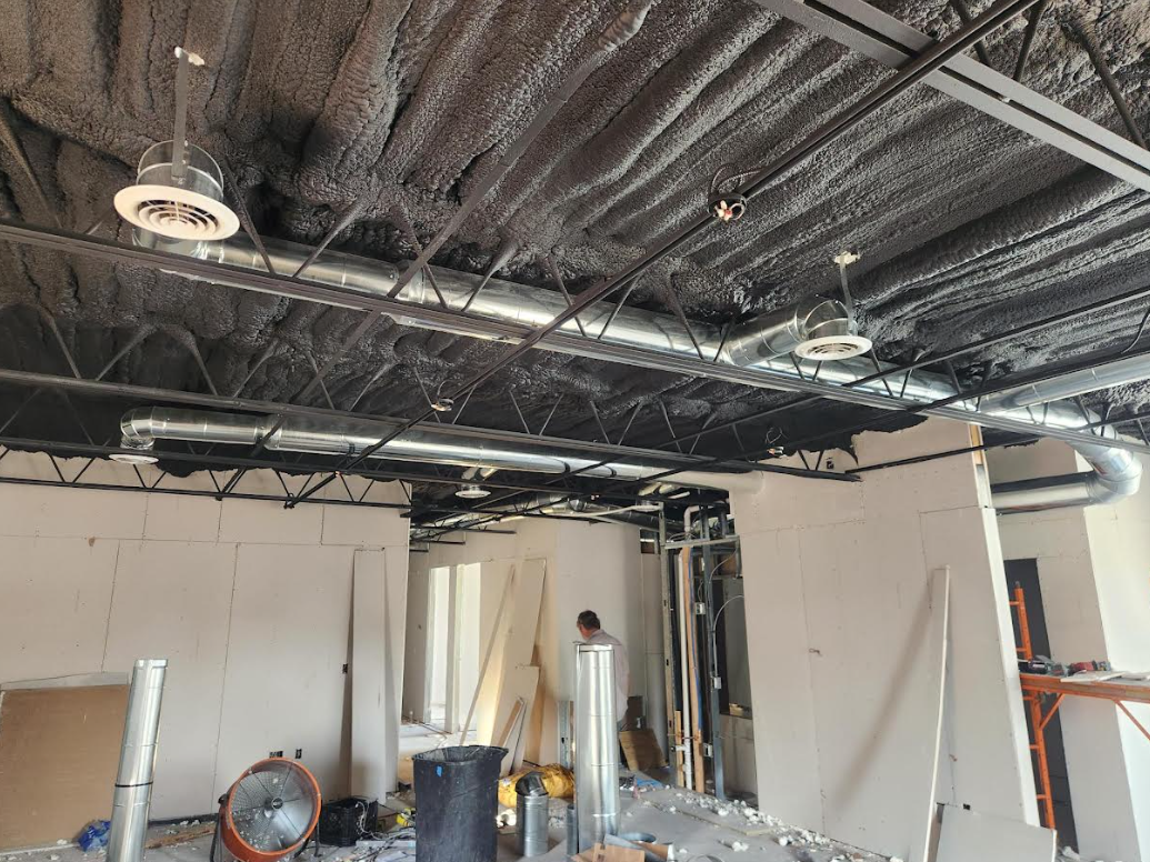 Construction site with exposed ceiling, hanging lights, and workers in a partially demolished room