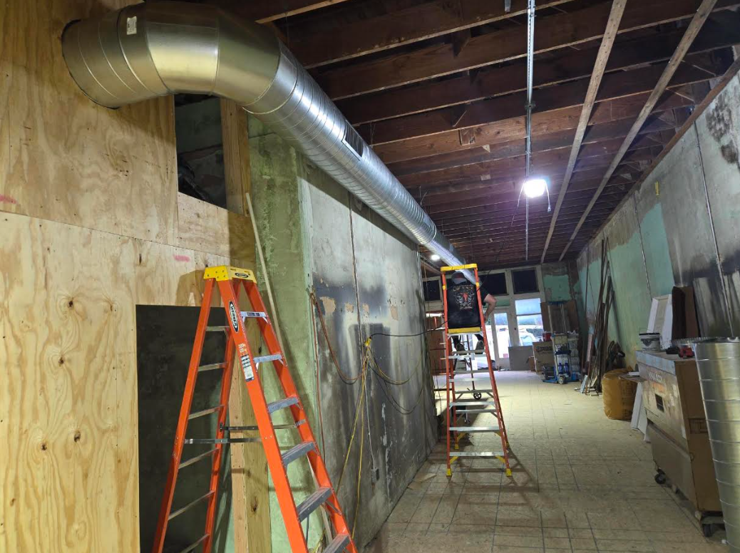 Basement remodel with ladders, exposed ductwork, and construction materials along a narrow hallway