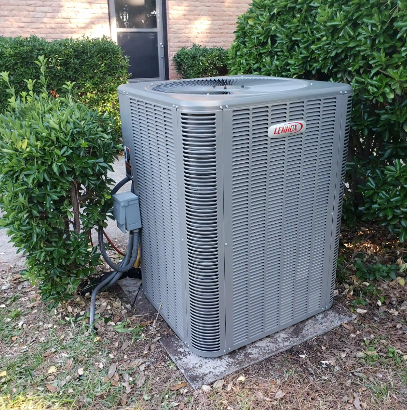 Outdoor HVAC unit beside shrubs and a brick house wall