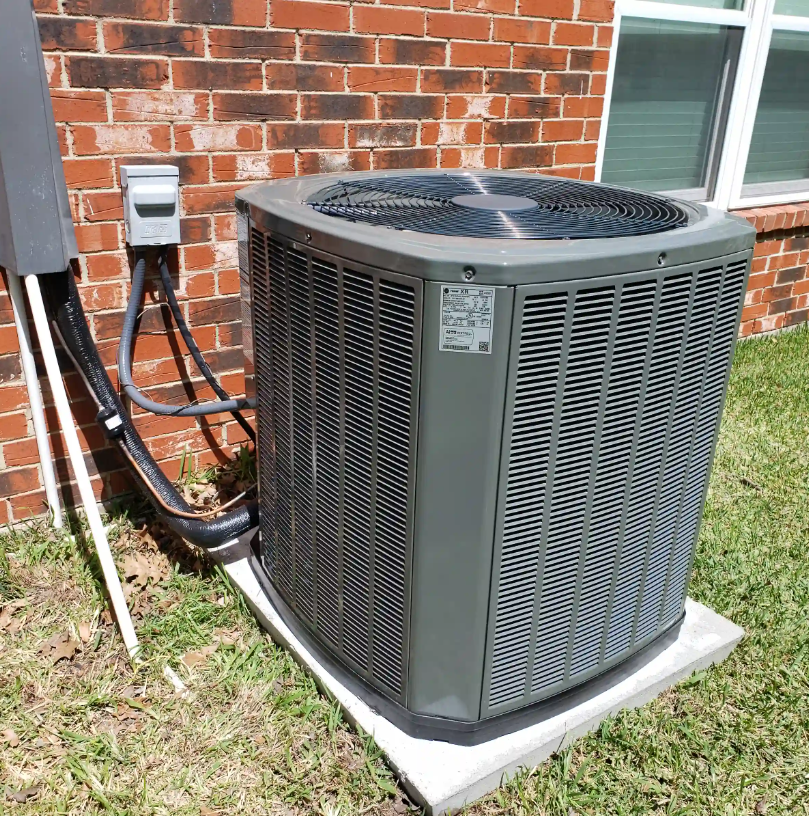 Outdoor air conditioning unit beside a brick house wall on a concrete pad