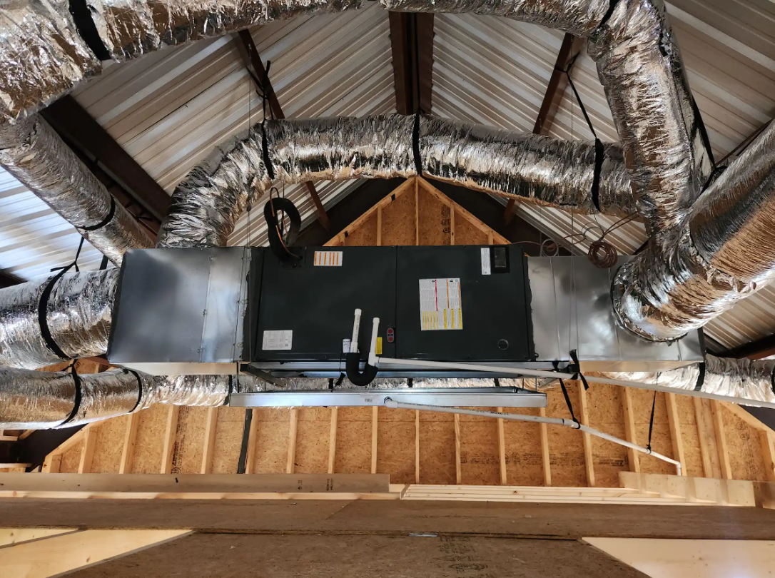 Attic with exposed insulation and HVAC ductwork above a wall-mounted unit.