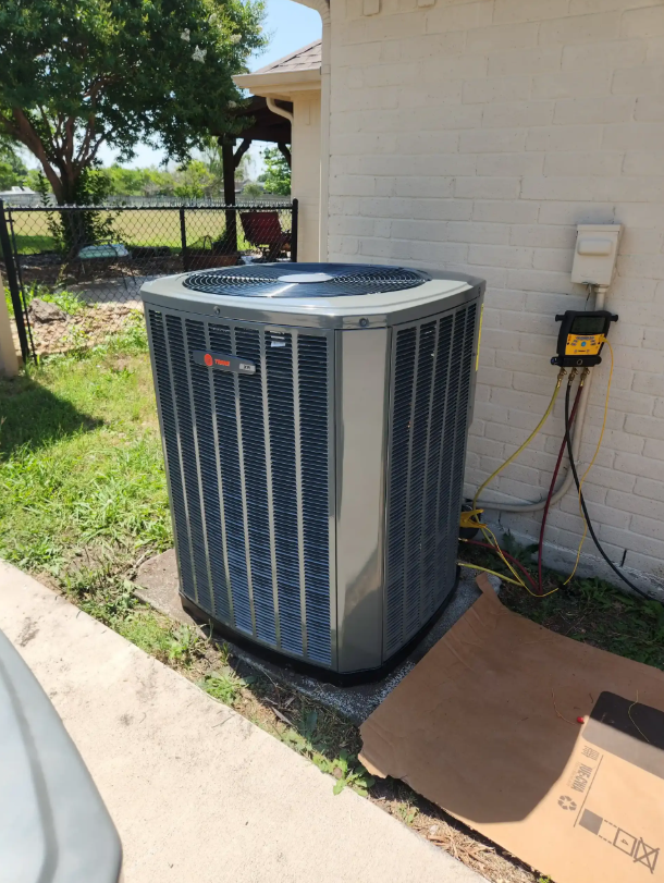 Outdoor air conditioner unit beside a house wall, with grass, sidewalk, and utility box nearby