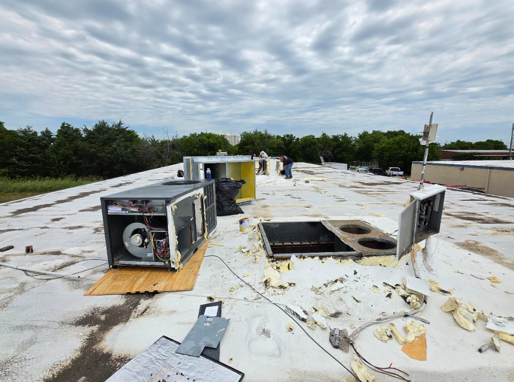 Rooftop with HVAC units on a white, weathered surface under a cloudy sky.
