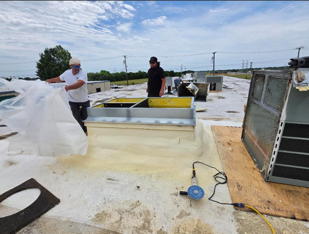 Workers on a flat rooftop applying a white waterproof coating beside HVAC equipment.