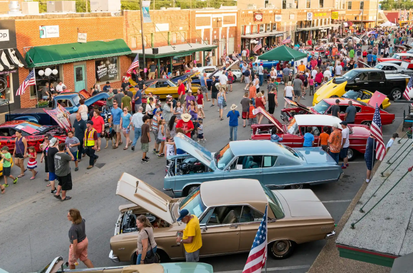 Crowded classic car show on a downtown street with vintage cars, spectators, and storefronts