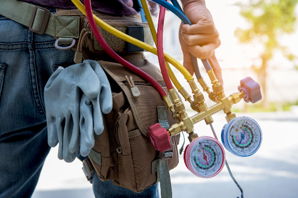 Person’s tool belt with gloves and HVAC gauges attached, with colorful hoses in a sunny outdoor setting