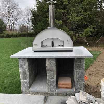 A pizza oven is sitting on top of a stone table in a backyard.