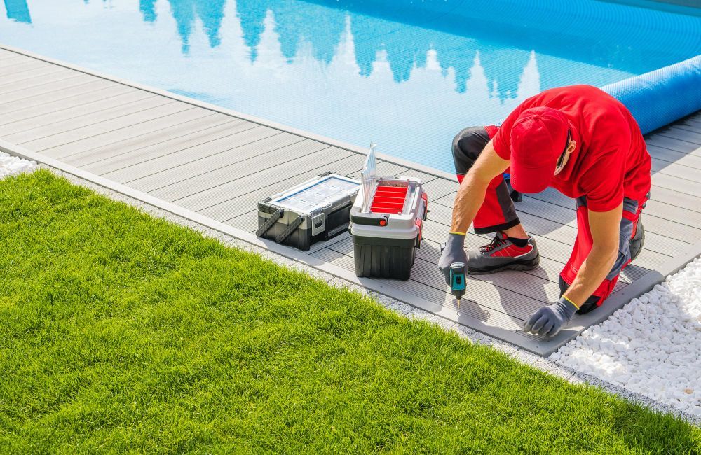 Worker in red shirt installing pavers beside a swimming pool and green lawn