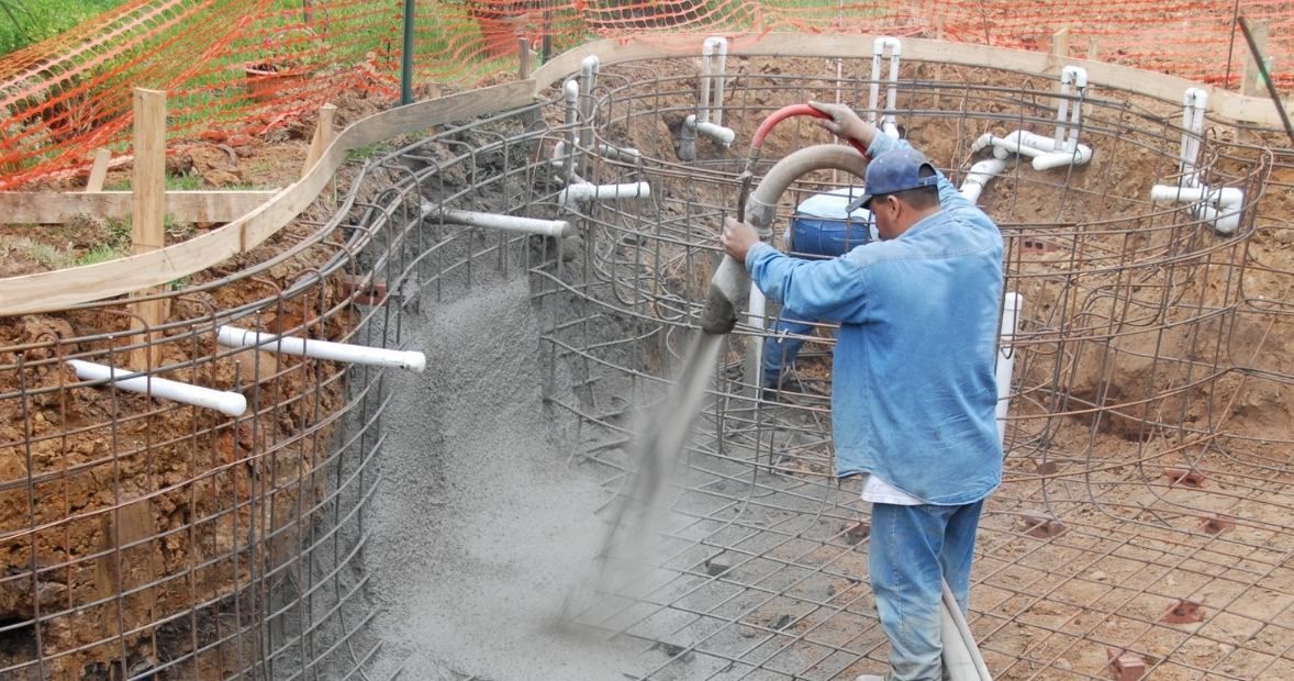 Worker spraying concrete onto a curved wall frame at a construction site