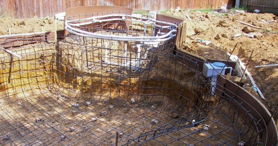 Excavation site with a large circular rebar foundation in a dirt pit, surrounded by soil and construction materials