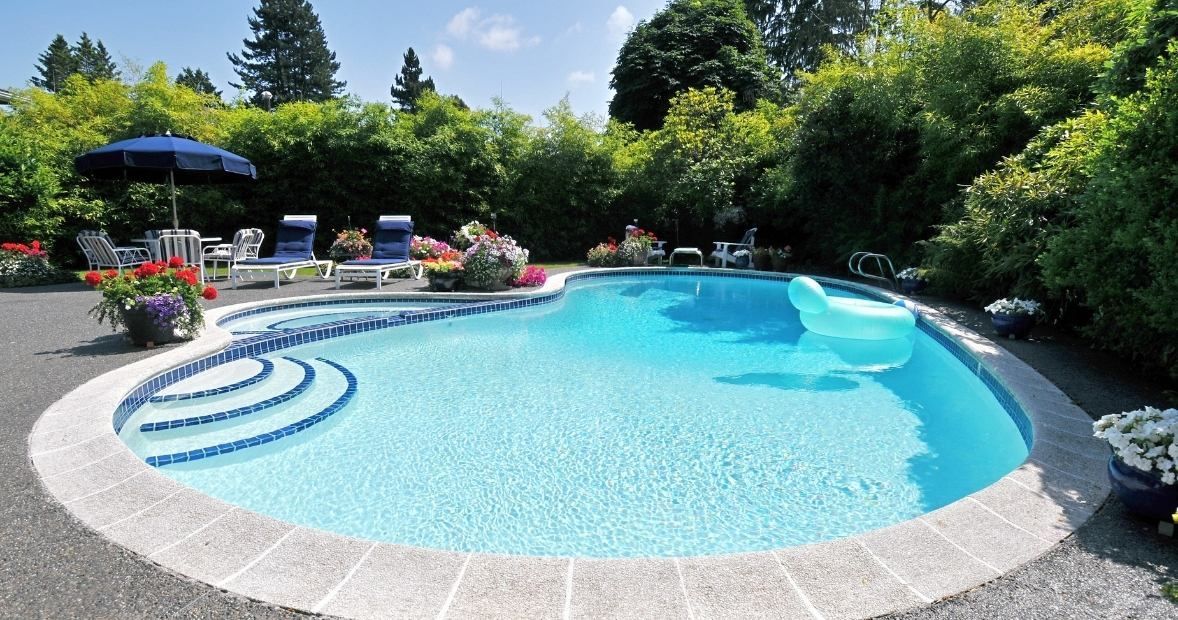 Backyard pool with blue water, curved steps, lounge chairs, umbrellas, and lush greenery around it
