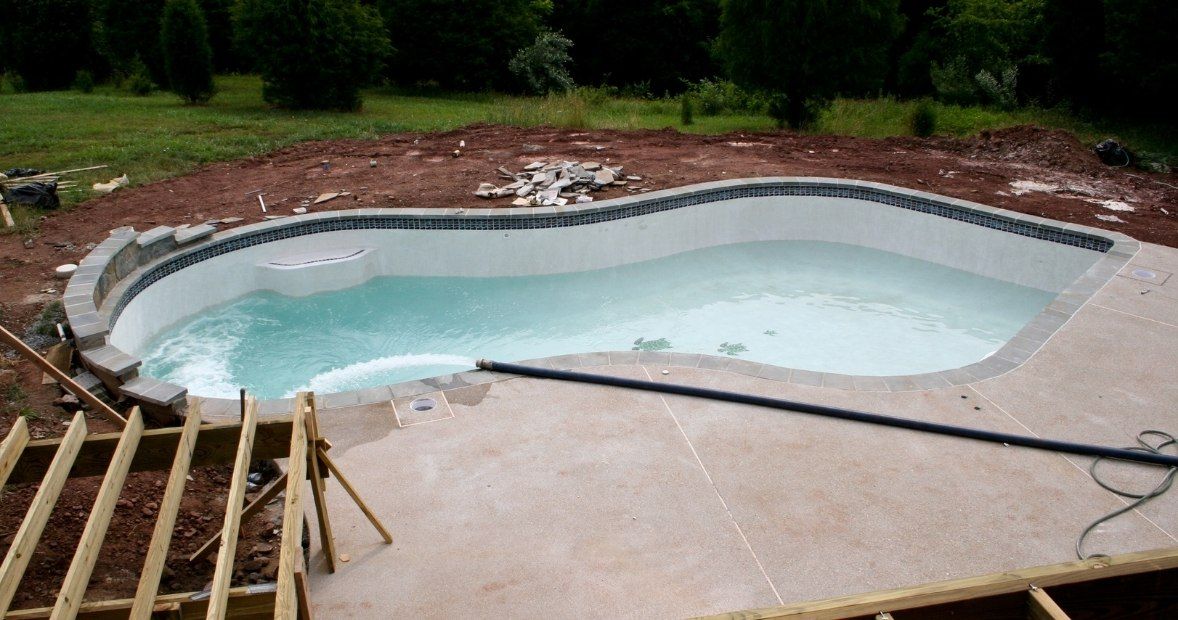 Partially built backyard swimming pool with concrete deck and wooden framing nearby