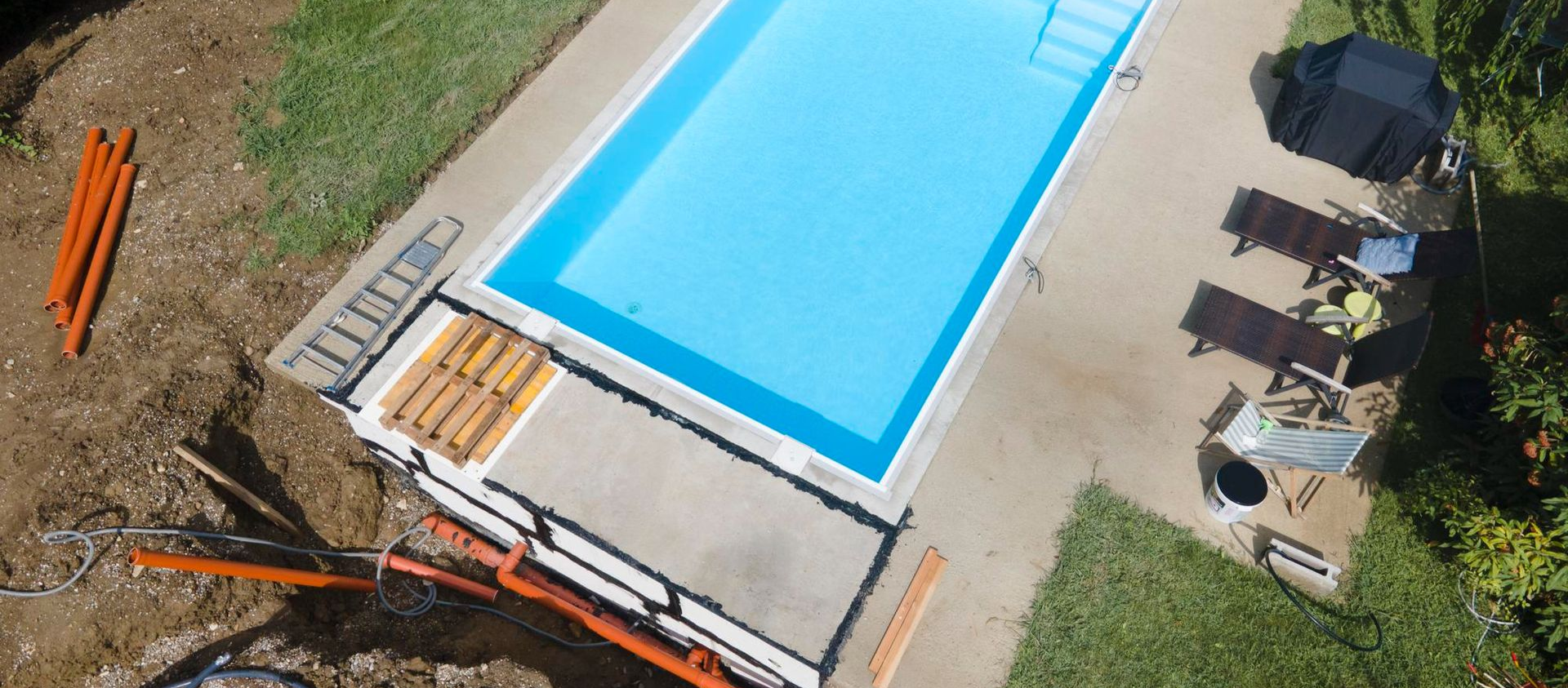 Aerial view of a backyard pool with patio chairs, a table, and a lounge chair on a sunny day