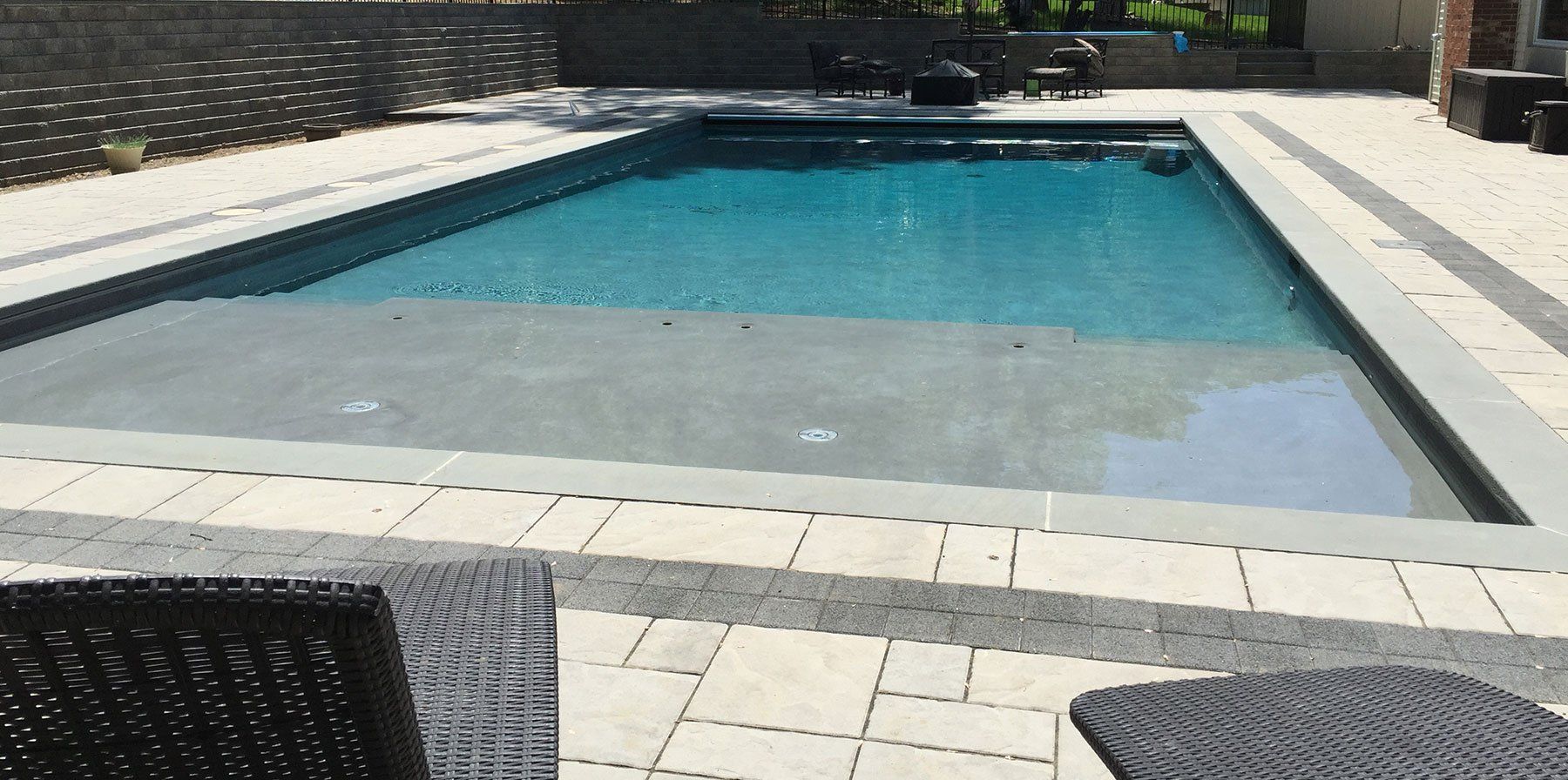 A large swimming pool is surrounded by a patio and chairs.