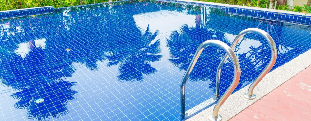 Blue-tiled swimming pool with a metal ladder and reflected trees on the water surface