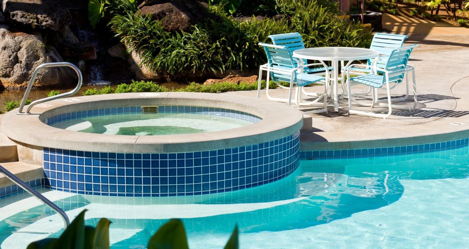 Blue-tiled poolside spa with turquoise water and white patio table and chairs nearby