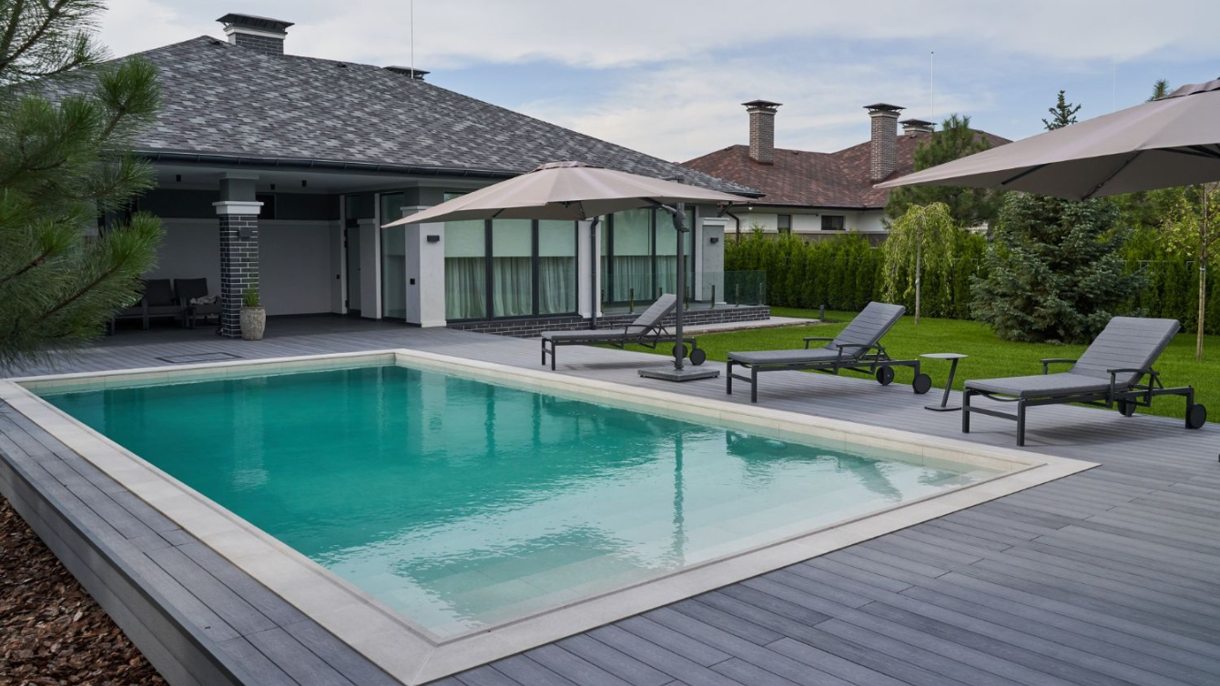 Modern backyard pool with lounge chairs, umbrellas, and a covered patio beside a house