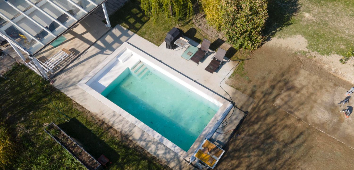 Aerial view of a rectangular swimming pool beside a stone patio and lounge chairs in a grassy yard