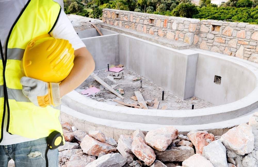 Kidney-shaped pool behind a contractor with construction helmet