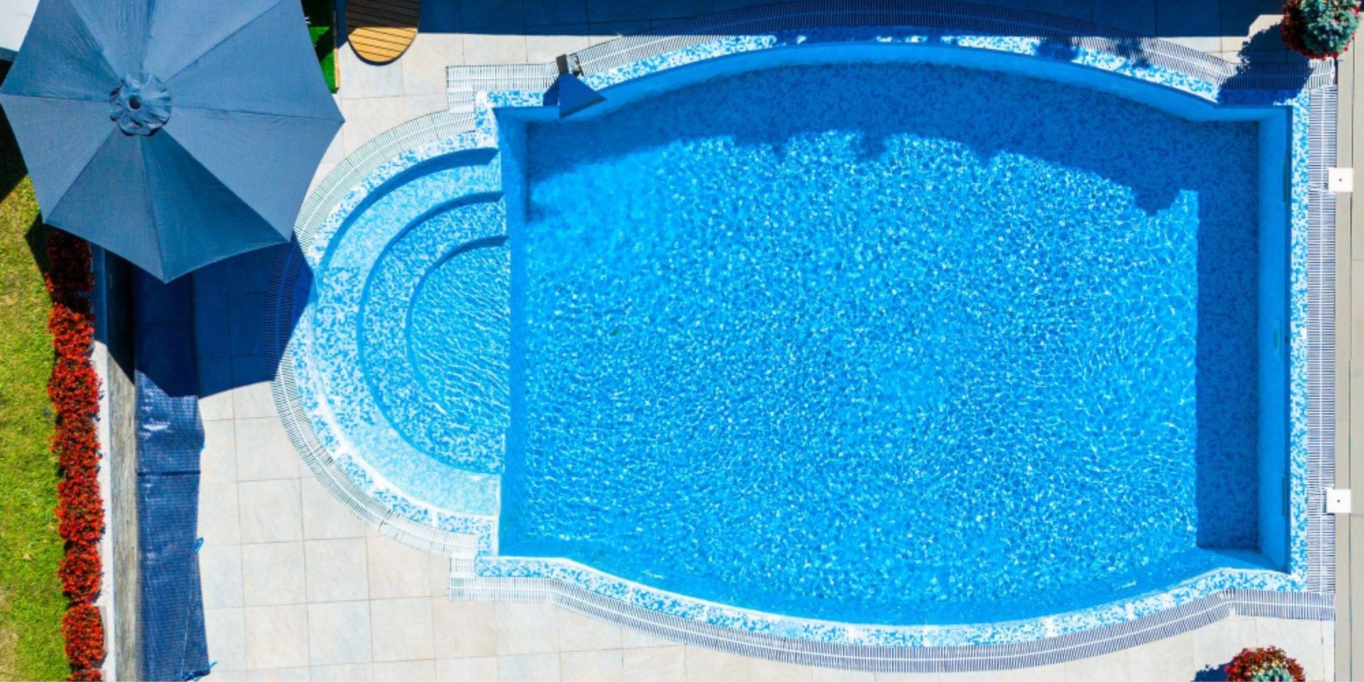 Blue swimming pool with curved spa and patio umbrella beside a tiled deck