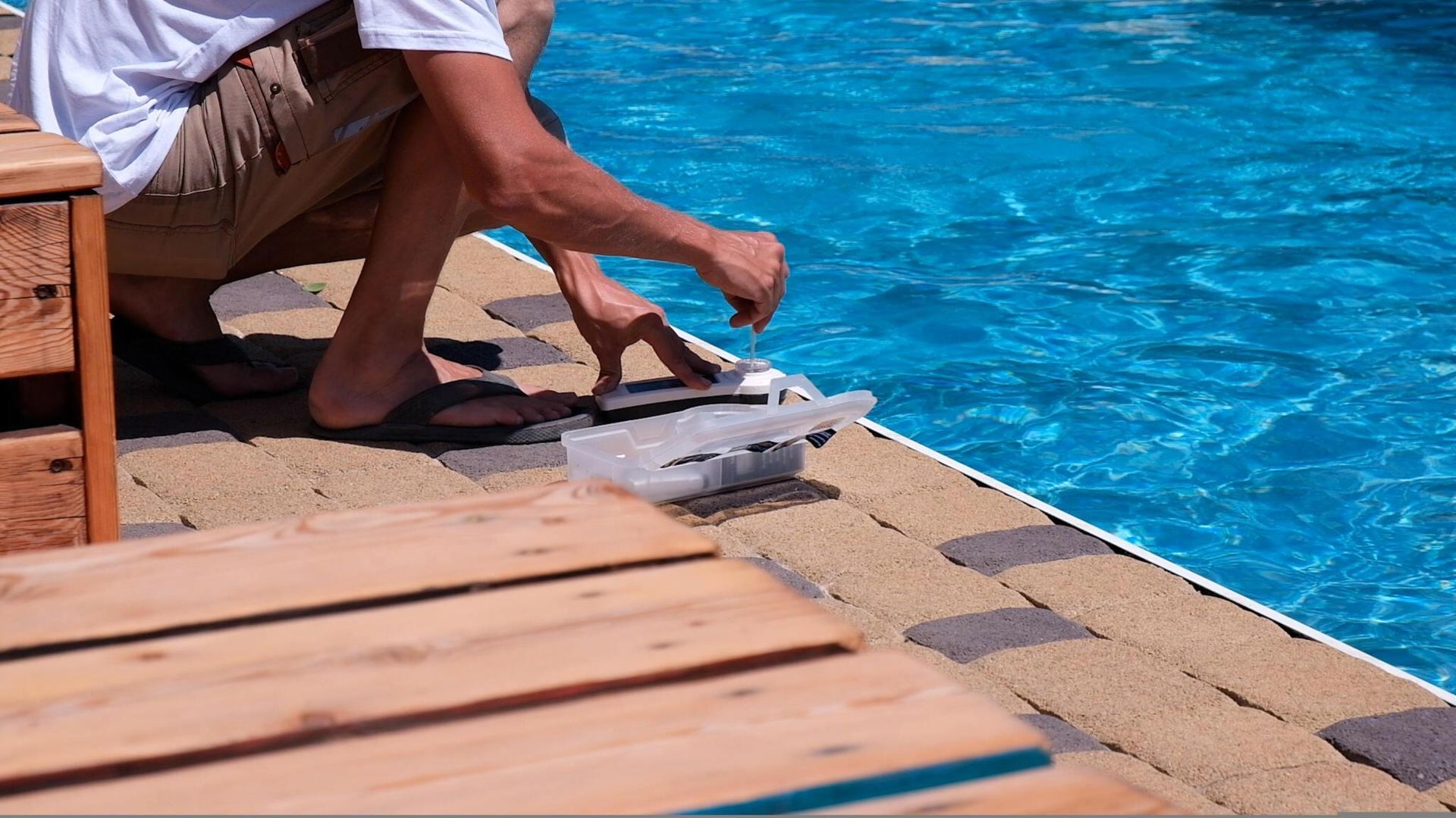 A man is kneeling next to a swimming pool.