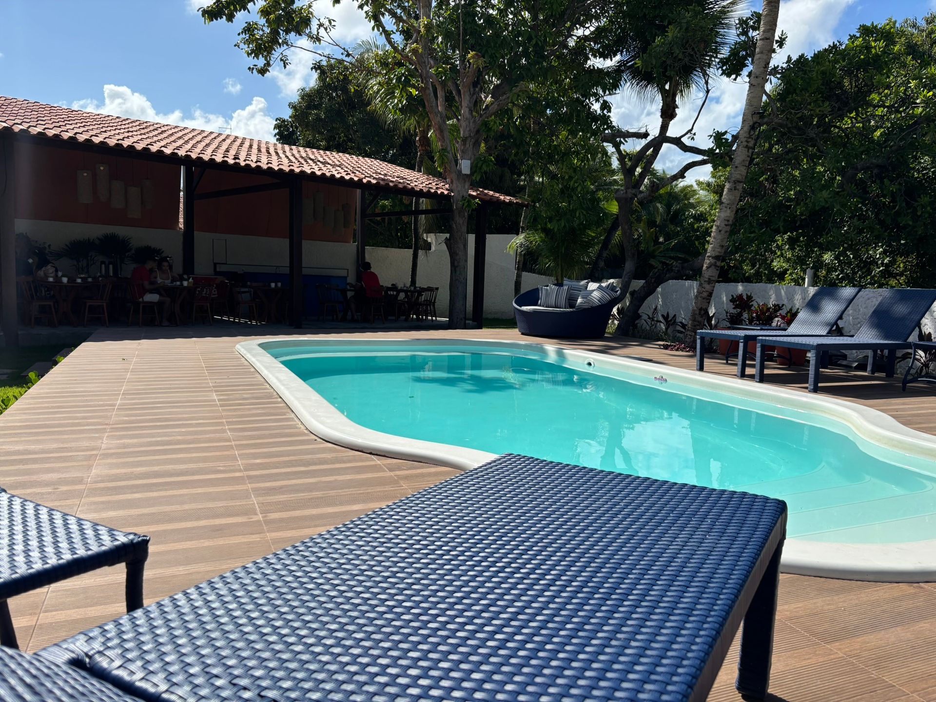 Uma grande piscina é cercada por cadeiras e um deck de madeira. Coralli Pousada