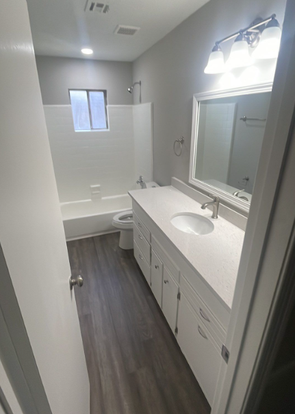 Bathroom with a white vanity, toilet, tub, and gray walls and flooring.