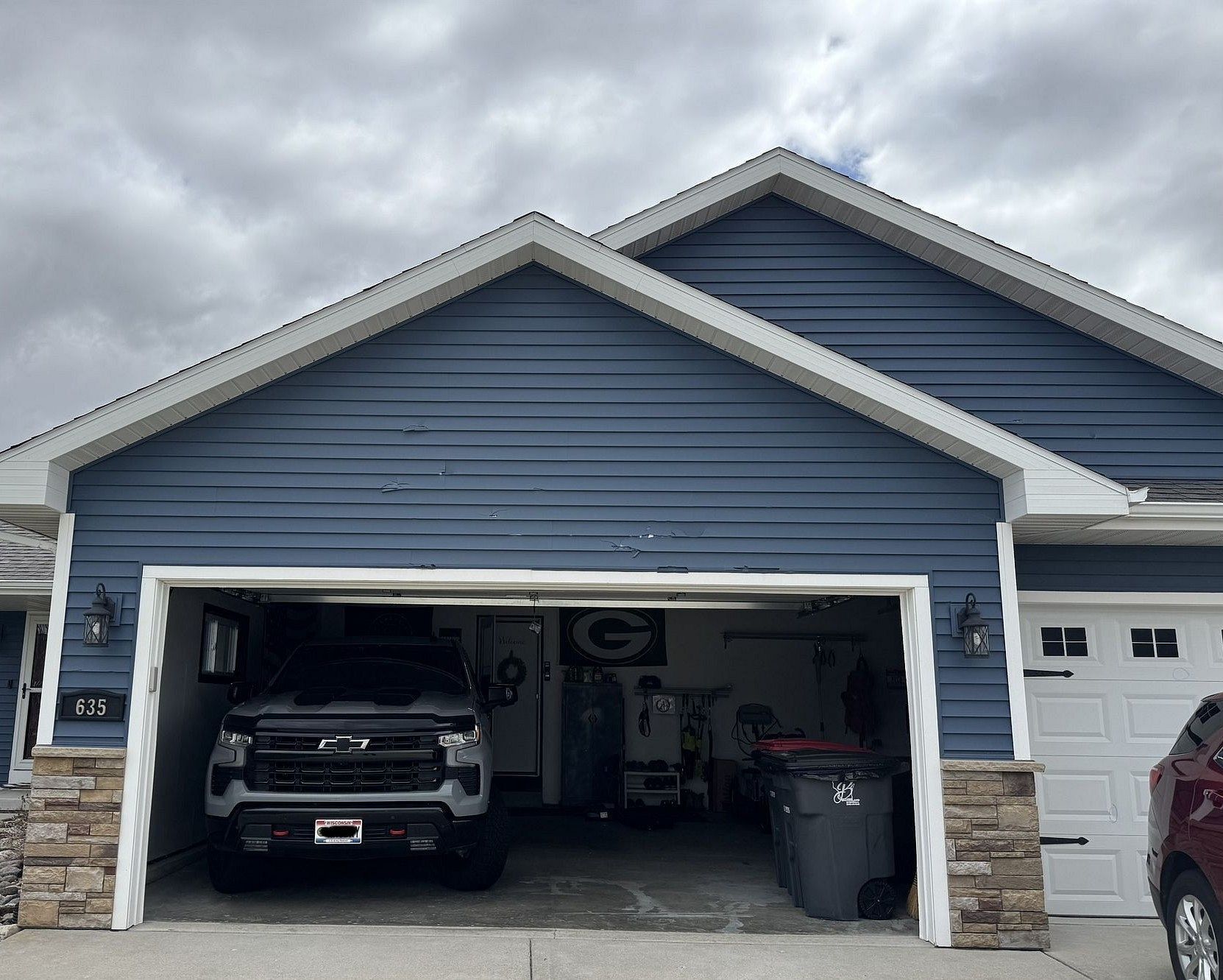 Blue house with open garage and black truck inside. Overcast sky.