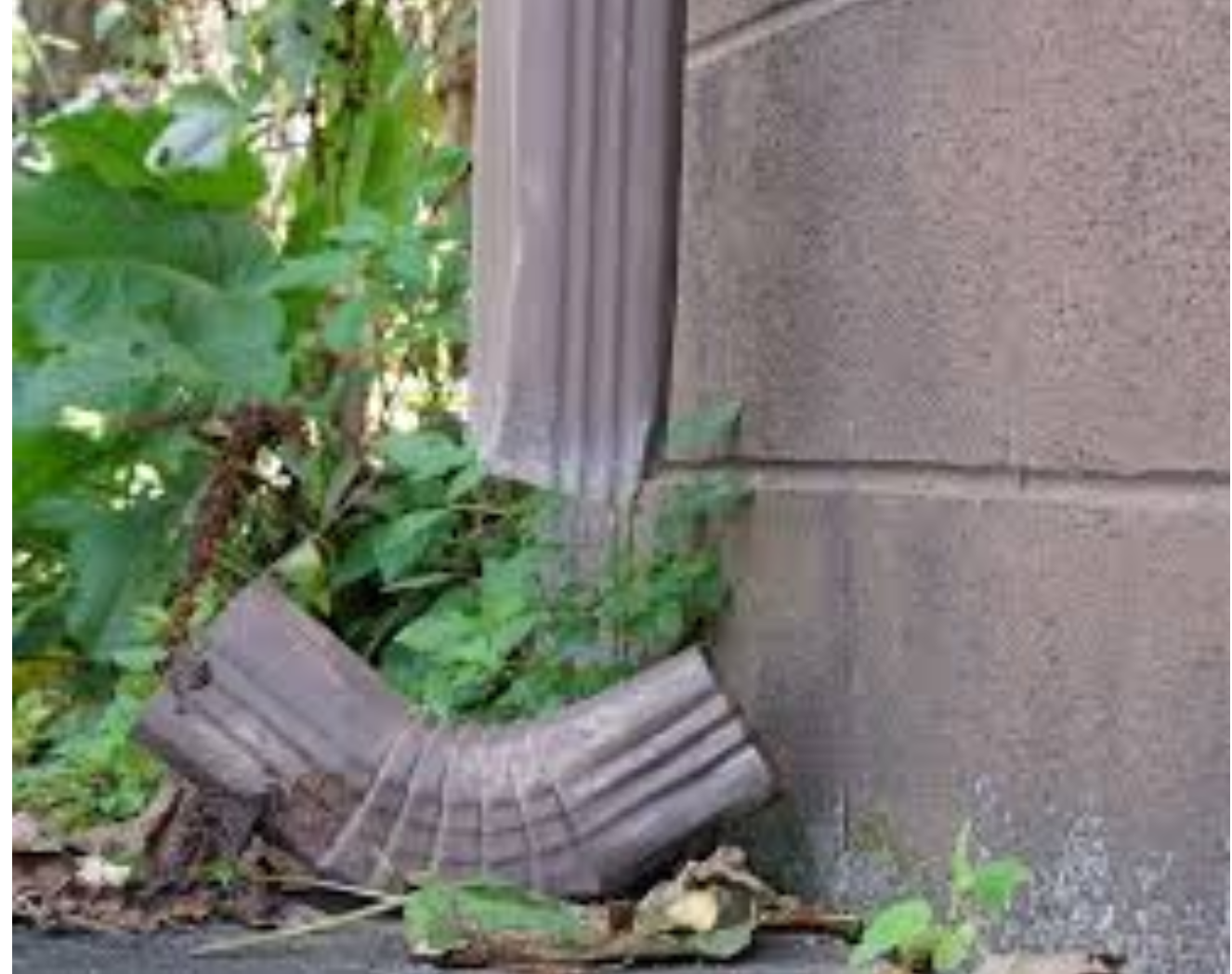 A broken gutter downspout is sitting on the ground next to a brick wall.