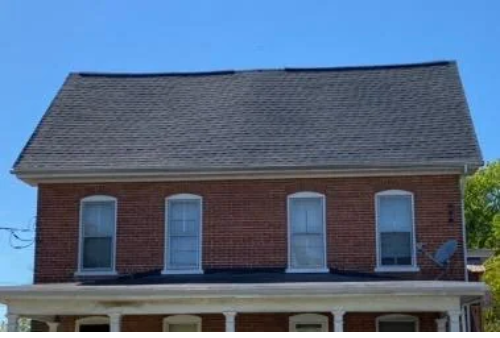 A large brick house with a sagging gray roof and many windows.