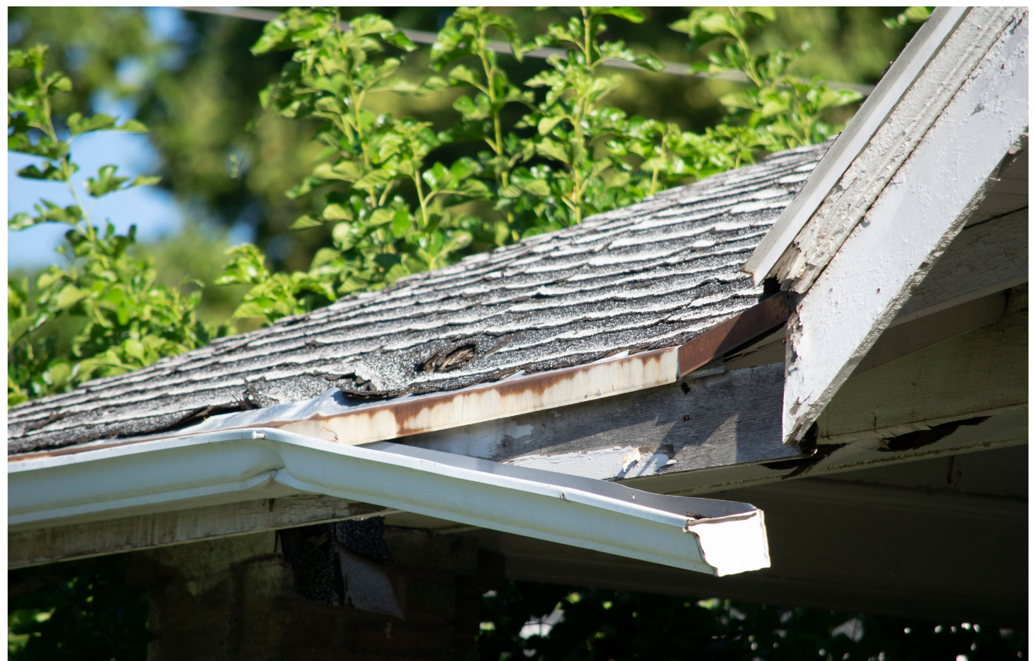 Damaged roof with peeling shingles and a broken gutter.