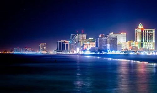 Nighttime city skyline with colorful lit buildings reflecting on calm water.