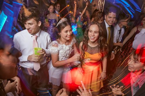 People dancing at a lively party, with colorful lights and drinks in hand.