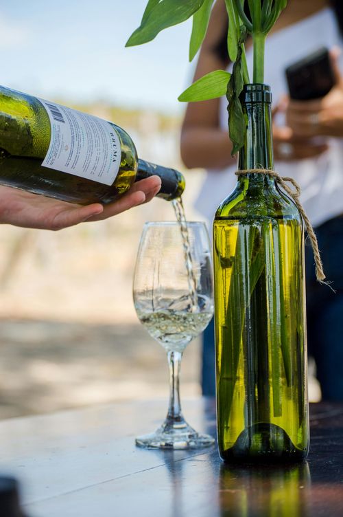 Wine being poured into a glass beside a green bottle on a table outdoors