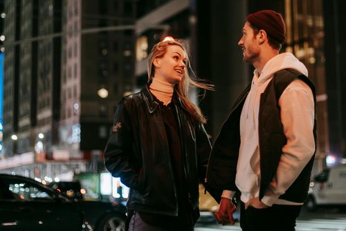 Two people talking on a city street at night, smiling under warm lights.