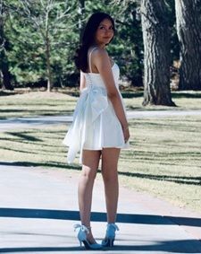 Woman in a white dress and blue heels standing on a park path, looking back near trees.