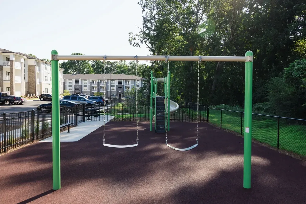 Playground with swings and a slide at a multifamily complex, green posts and a safety surface.