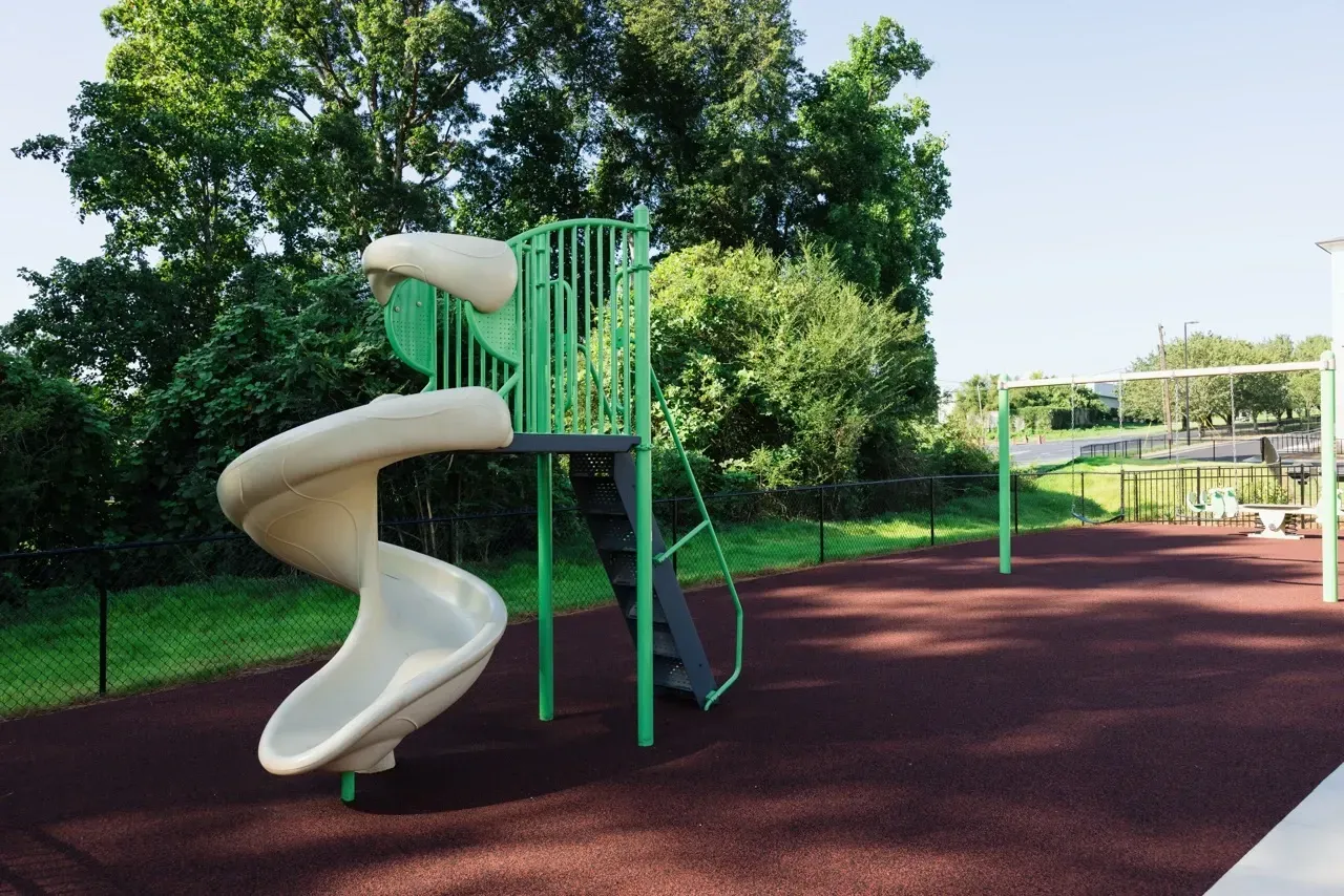Playground with beige spiral slide and green climbing structure on a red safety surface.